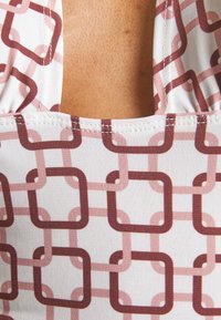 Top de roupa de banho com um padrão geométrico em tons de burgundy e blush sobre um fundo branco, com tecido suave e bordas cosidas.