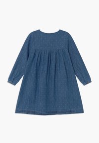 Vestido de mezclilla con mangas largas, escote redondo, cintura fruncida y estampado de lunares blancos. Presenta puños abotonados y un bajo a la altura de la rodilla.