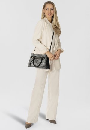 Black and white logo-printed handbag with a structured shape, contrasting textures, and a long shoulder strap, paired with a light-colored outfit.