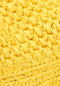 Gros plan sur un matériau en paille ou raphia jaune vif tissé étroitement avec un motif tressé épais et texturé.