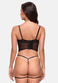 Mustatyöpesetti, joka sisältää läpinäkyvän raidallisen bodysuitin, jossa on hakas sulku ja säädettävät hihnat, ja joka on täydennetty vastaavilla stringeillä.