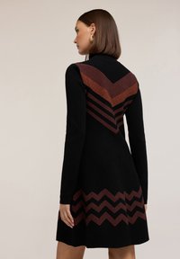 Abito nero con maniche lunghe, caratterizzato da un motivo a zig zag testurizzato in marrone e ruggine sul corpino e sull'orlo, con una silhouette aderente.