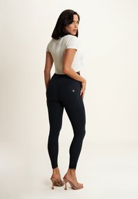 Leggings neri con vita alta e dettagli delle cuciture curve, realizzati in tessuto elasticizzato. Abbinati a una maglietta corta bianca e tacchi nudi.