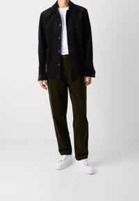 Czarna kurtka z korduroyu z dwiema przednimi kieszeniami, w połączeniu z ciemnozielonymi spodniami z korduroyu. Biała koszulka i białe trampki dopełniają całość.