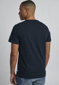 Mørkeblå bomulds T-shirt med korte ærmer, rund halsudskæring og et diskret mærke på venstre sidesøm. Glat tekstur, tætsiddende design.