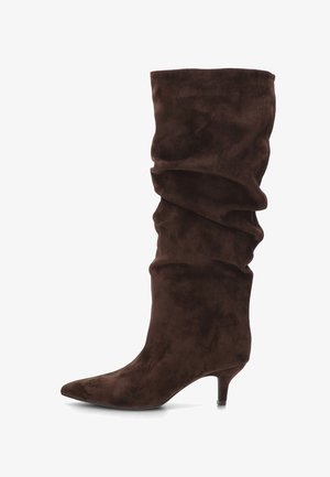 Bota hasta la rodilla de gamuza marrón con diseño holgado, punta puntiaguda y tacón cónico, con textura suave y pliegues caídos.