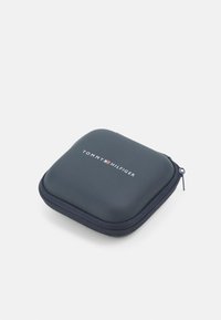 Kompakti tummansininen vetoketjullinen kotelo, jossa on matta pinta ja valkoinen "TOMMY HILFIGER" -logo yläpinnalla. Neliön muotoinen.
