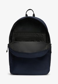 Mochila azul marino de forma redondeada, con interior negro, compartimentos con cremallera y un bolsillo delantero. Cuenta con una tela duradera y cremalleras dobles.