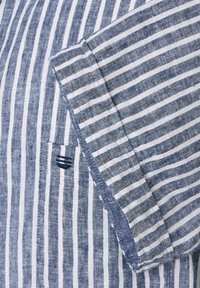 Blauw-wit gestreepte shirt met een linnenstructuur, voorzien van een zak en contrasterende stiksels op de kraag en mouwranden.