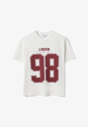 Camiseta blanca de cuello en V con un gran número "98" en color burdeos y el texto "London World Tour" encima del número en la parte delantera.