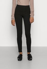 Leggings negros ajustados con cintura alta y material elástico. Combinados con zapatos negros de tipo slip-on con una hebilla decorativa.