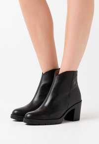 Schwarze Leder-Stiefel bis Knöchel mit glattem Finish, runden Zehen, einem Blockabsatz in mittlerer Höhe und strukturierten Gummisohlen.
