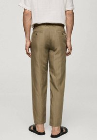 Volné khaki pruhované kalhoty s kapsami vzadu a plochým předním dílem, nošené s černými sandály. Lehké látky, ležérní styl.