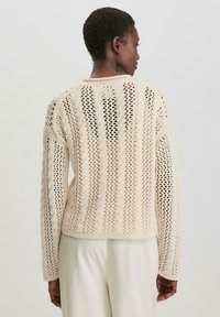 Strickpulli in Creme mit einem offenen, strukturierten Muster. Verfügt über lange Ärmel und einen verkürzten Saum, der ein Zopfmuster-Design präsentiert.
