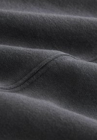 Tmavě šedá látka s jemným, texturovaným povrchem a viditelnými švy. Materiál vypadá lehce a mírně elasticky.