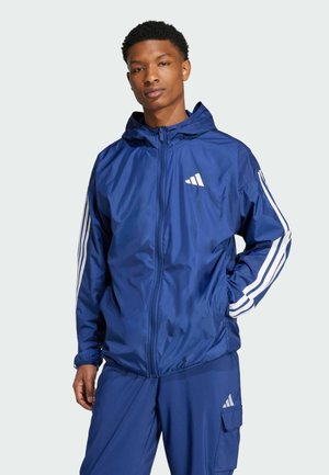 Veste à capuche bleue avec des accents blancs, présentant une fermeture éclair à l'avant, des poignets élastiques et trois rayures blanches sur les manches. Fabriquée en tissu lisse.