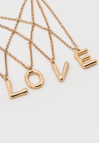 Τέσσερα χρυσά κολιέ αλυσίδας με γράμματα-μενταγιόν που σχηματίζουν τη λέξη "ΑΓΑΠΗ" σε λευκό φόντο.