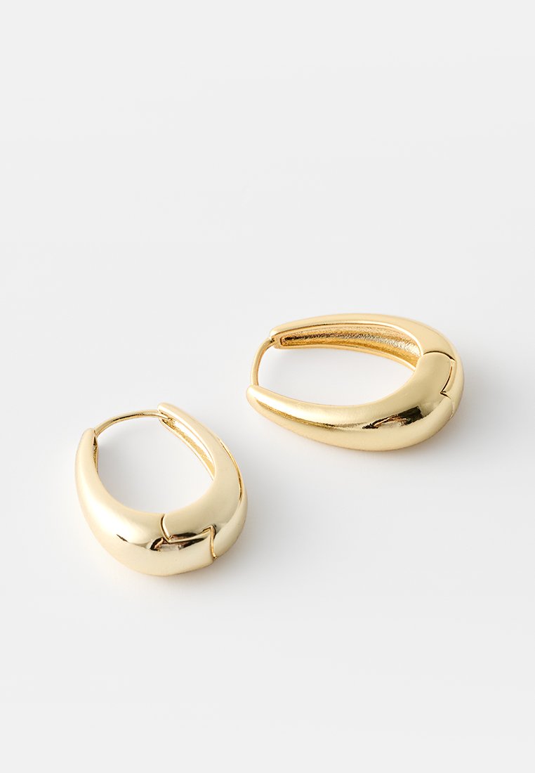 Goldene Creolenohrringe mit einer glatten, polierten Oberfläche und einem geschwungenen Design, das oben eine kleine Aussparung aufweist.