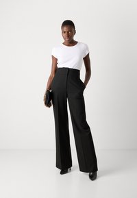 Pantalons noirs taille haute avec des jambes larges, associés à une chemise blanche ajustée à manches courtes. Une pochette noire et des talons complètent le look.