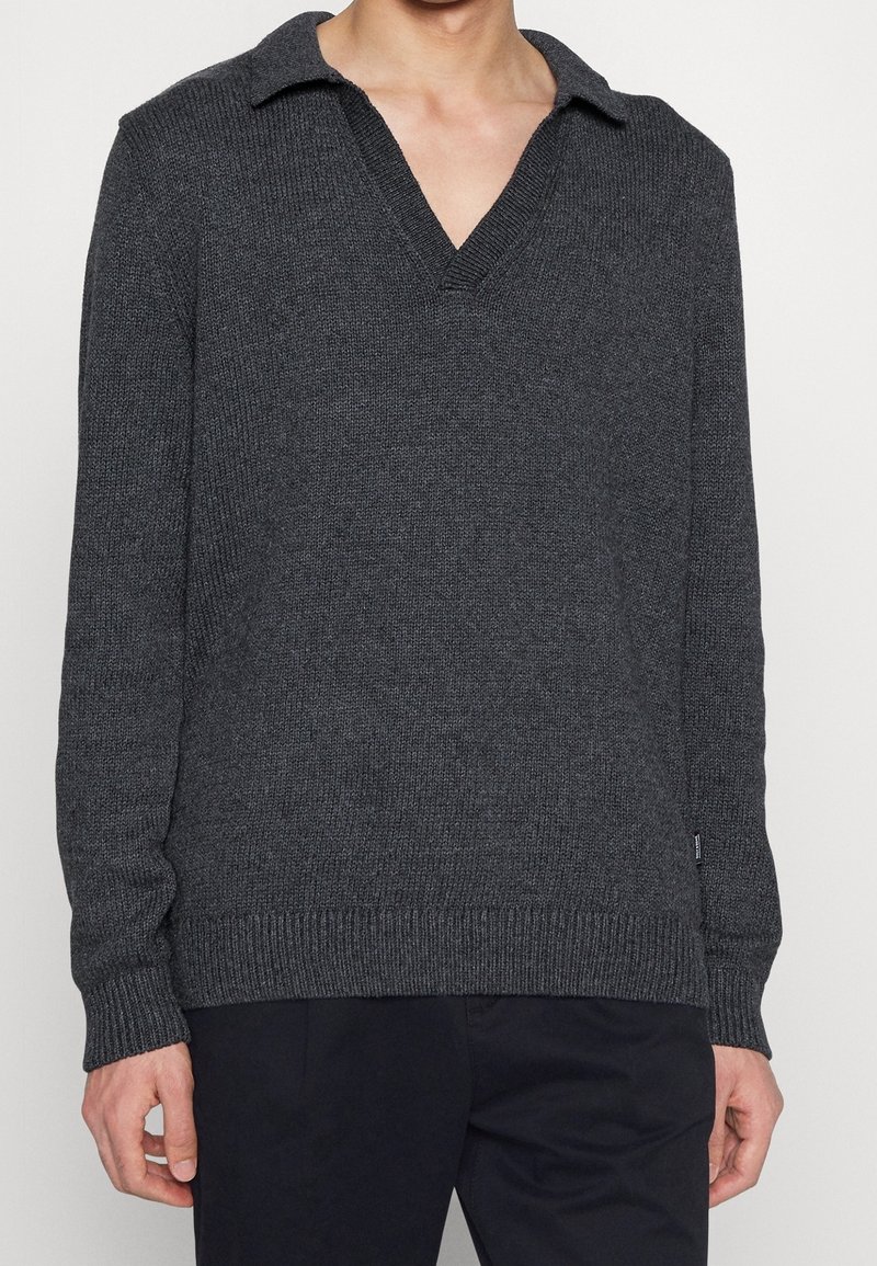 Pull en tricot gris foncé avec un col en V. Dispose de poignets et d'un ourlet côtelés, mettant en valeur un tissu texturé.
