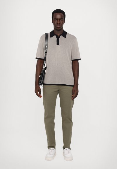 Kortermet, ribbet polo i grå, med marineblå krage og mansjetter. Kombinert med olivengrønne bukser og hvite sneakers, holder en svart veske.