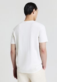 T-shirt bianca a maniche corte con collo rotondo realizzata in un tessuto testurizzato, caratterizzata da una vestibilità comoda e cuciture sottili sul retro.