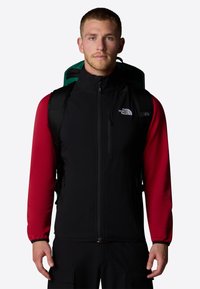 Gilet pour homme avec un devant noir et des manches longues rouges, présentant un col montant, des poches zippées et une texture de tissu durable.