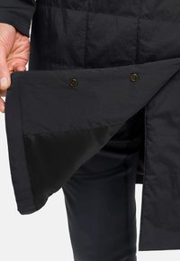 Zwarte pufferjackstof met een gestikt ontwerp. Het interieur heeft een gladde zwarte voering en bruine drukknoopsluitingen.