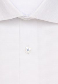 Gros plan d'une chemise blanche à col avec un seul bouton blanc fermé au centre sous le col.