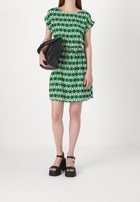 Green dress with geometric black and green pattern, short sleeves, cinched waist, paired with a black shoulder bag and platform shoes.