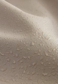 Beige Stoff mit einer glatten Textur, auf dessen Oberfläche sich Wassertropfen verschiedener Größen befinden, die auf Wasserbeständigkeit hinweisen.