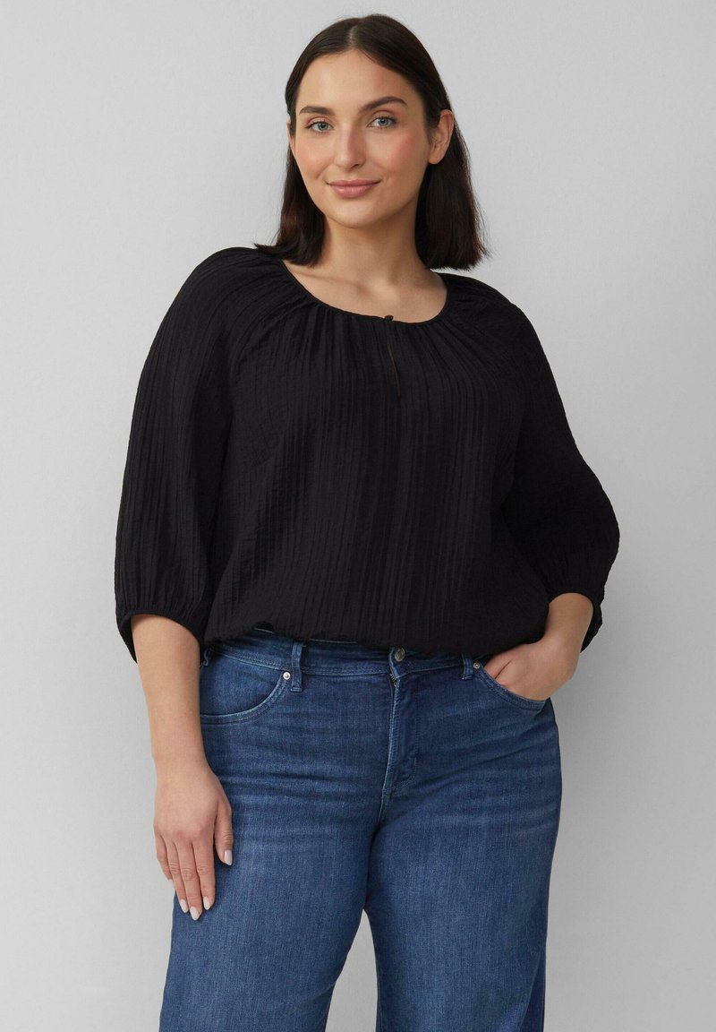 Zwarte, gestructureerde top met een ronde halslijn en driekwart mouwen, gecombineerd met blauwe denim jeans. Belangrijke details zijn verticale strepen op de stof.