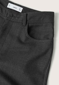Pantalons en tissu gris foncé avec poche avant, passants de ceinture, bouton noir et étiquette de marque MNG visible à l'intérieur de la ceinture.