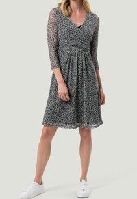 Vestido tipo envoltura en blanco y negro con mangas tres cuartos, cintura ceñida y un patrón de hojas, combinado con zapatillas blancas.