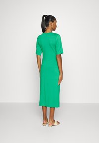 Vestido verde de comprimento médio feito de tecido suave, com mangas curtas e corte reto, apresentando um decote redondo e fendas laterais.