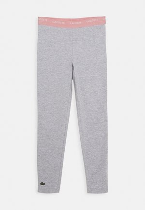 Leggings grigi con un elastico rosa in vita che presenta il testo "LACOSTE" e il logo verde del coccodrillo vicino all'orlo in fondo sulla gamba sinistra.