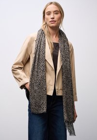 Sciarpa beige con motivo leopardato nero, in tessuto leggero e con bordi sfilacciati, indossata sopra una maglietta scura e jeans.