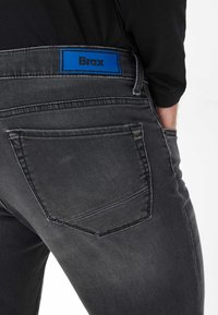 Jeans in denim grigio con una cintura blu brandizzata, dotati di tasche posteriori con cuciture sottili e una texture morbida.