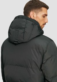 Czarna kurtka puchowa z kapturem, charakteryzująca się grubą, pikowaną strukturą i regulowanymi paskami na kapturze. Prosty, nowoczesny design.