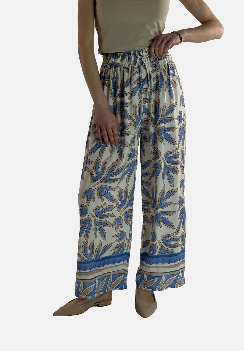 Vloeiende, crèmekleurige broek met een blauw bloemenpatroon. Elastische tailleband en wijde benen. Gecombineerd met lichtbeige schoenen.