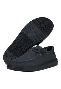 Zapatillas de lona negras con una suela de goma suave que presenta un agarre texturizado y un discreto patrón de estrellas, complementadas con un cierre de cordones.