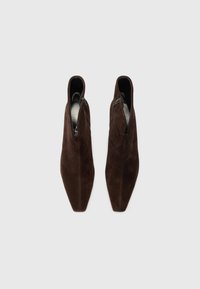 Bottines en suede marron avec un bout pointu, une fermeture éclair sur le côté et une doublure intérieure lisse. Présente un design épuré et une semelle plate.