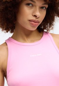 Ροζ ριμπ φανέλα με στρογγυλή λαιμόκοψη, με λευκό λογότυπο "Calvin Klein" μπροστά. Λείος υφή και εφαρμοστή σχεδίαση.