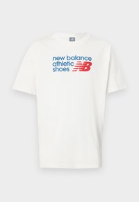 Fehér pamut póló, rövid ujjakkal. Kék és piros szöveggel ellátott, amely az "új egyensúly sportcipők" feliratot tartalmazza, valamint a New Balance logója.