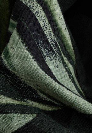 Pletená tkanina s tmavě zelenými a černými pruhy, zdobená texturovaným vzorem. Materiál vypadá měkce a mírně chlupatě.