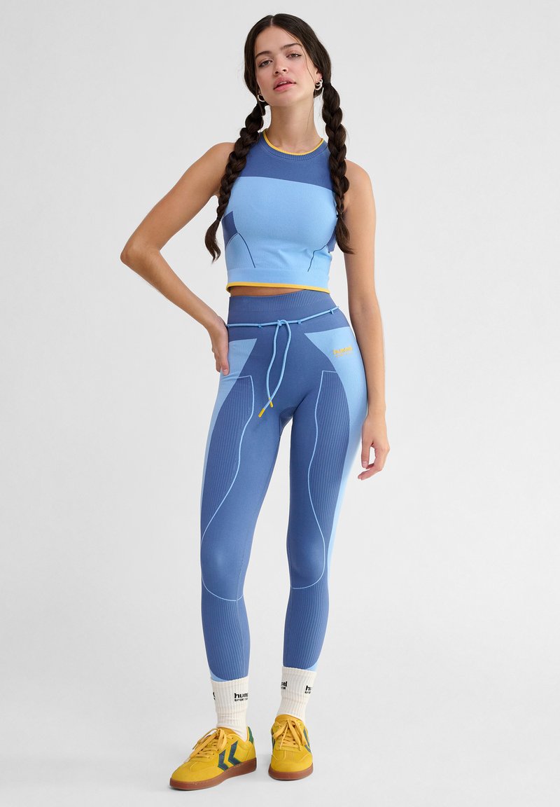 Niebieski sportowy crop top z żebrowanej tkaniny, w połączeniu z dopasowanymi legginsami o wysokim stanie, z blokowaniem kolorów i detalem w postaci sznurka.