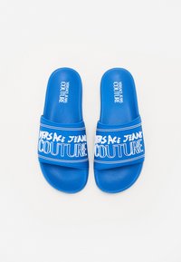 Mėlynos šlepetės, pagamintos iš sintetinių medžiagų, su tekstūruota apdaila ir dideliu baltu logotipu, kuriame užrašyta "VERSACE JEANS COUTURE".