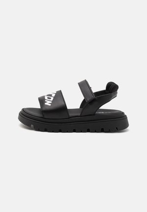 Sandalias negras con dos correas anchas, cierres ajustables de Velcro y una suela gruesa y texturizada. Presenta un logotipo blanco en la correa superior.