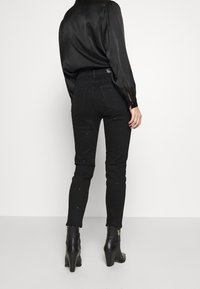 Černé džíny z denimu s úzkým střihem, zdobení hroty, vysokým pasem a zadními kapsami, kombinované s černou saténovou blůzou a kotníkovými botami.