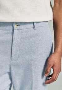 Hellblaue Hose aus strukturiertem Stoff, mit einem Knopfverschluss und Seitentasche, im lässigen Schnitt und maßgeschneiderter Passform.
